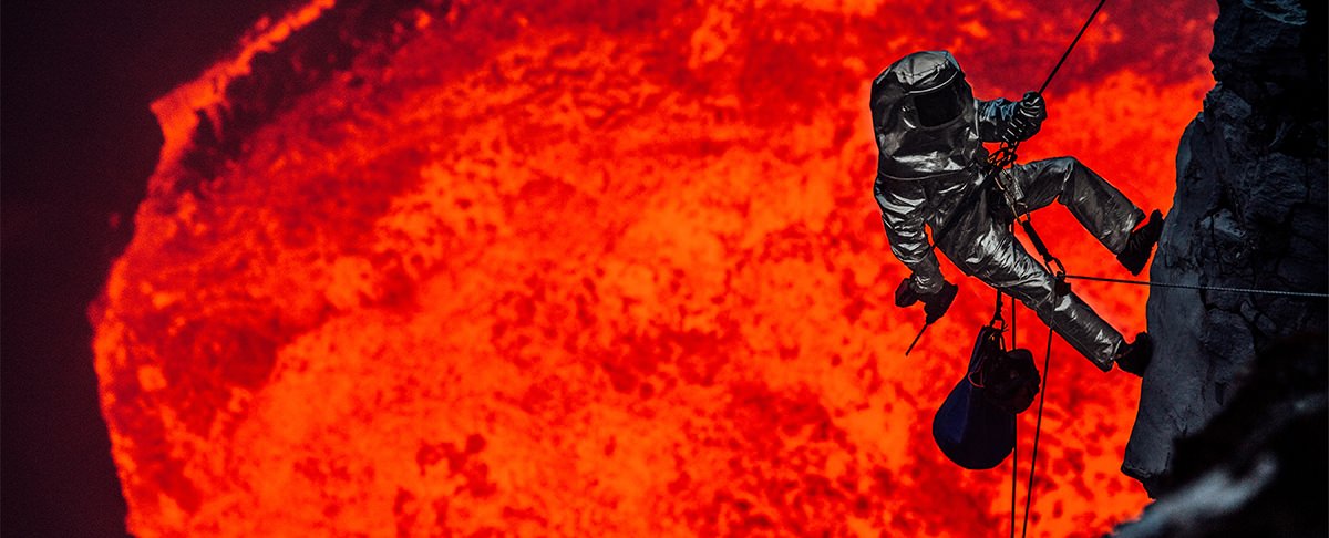 The Volcano Diver repelling into a lava lake wearing Newtex Proximity Suit Background Image